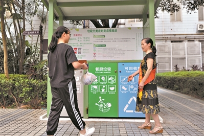 天河区石牌街穗园小区党员汤晓兰在定时定点垃圾分类投放点前站桶，指引居民垃圾分类。