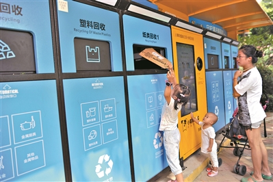 荔湾区海龙街紫林香苑小区，居民带着小朋友在小黄狗智能垃圾分类机器前分类投放垃圾。