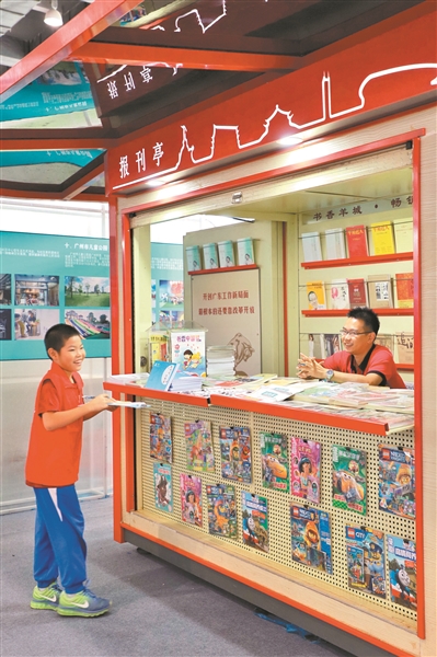 一位小朋友在向报刊亭里的工作人员咨询智能报刊朗读亭的功能。 